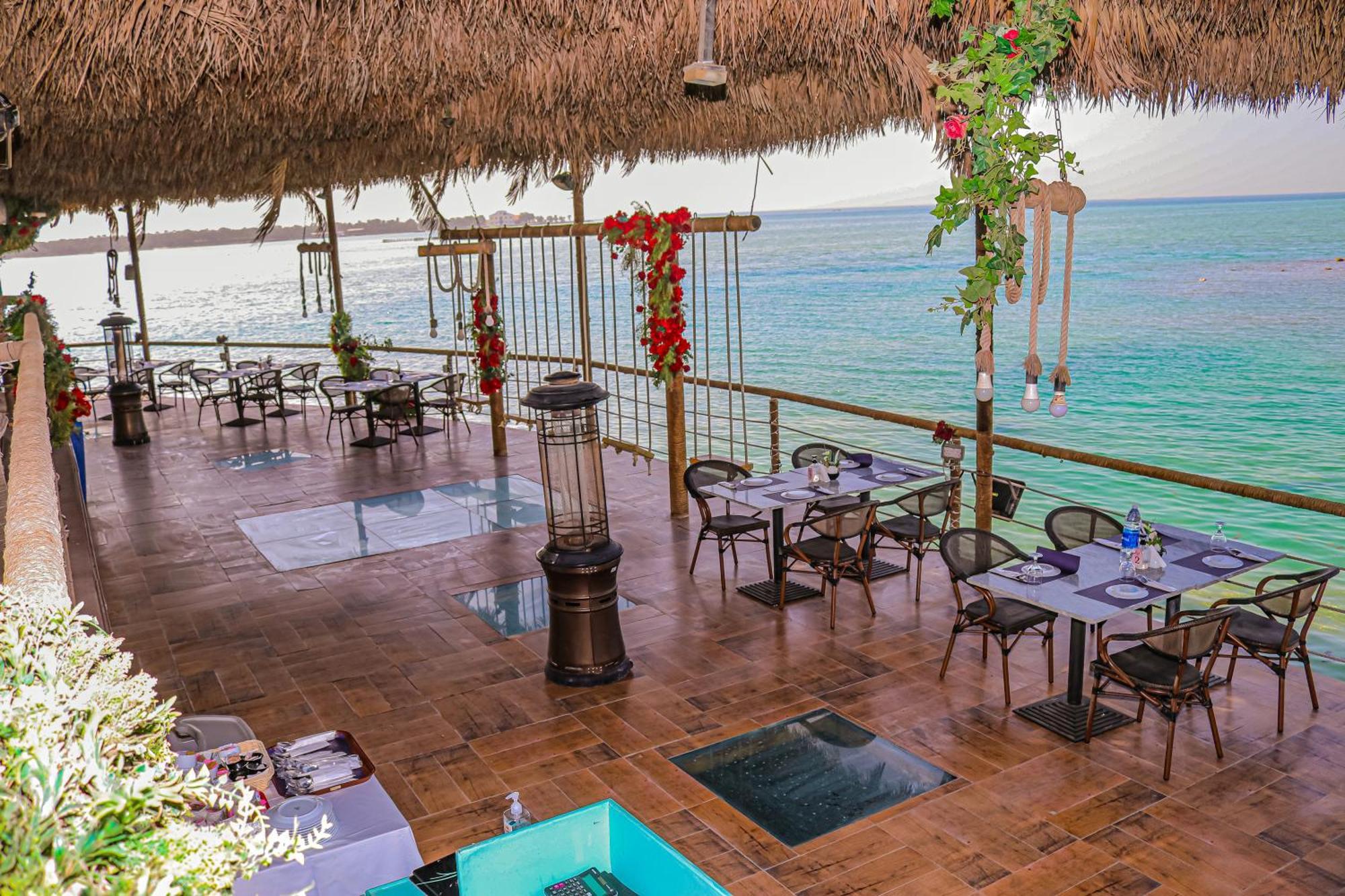 Lagoona Beach Luxury Resort And Spa Μανάμα Εξωτερικό φωτογραφία The photo depicts a coastal restaurant or dining area with an open-air design. It features a wooden floor and tables set for dining, surrounded by chairs. The space is partially covered by a thatched roof, providing shade while allowing for a view of