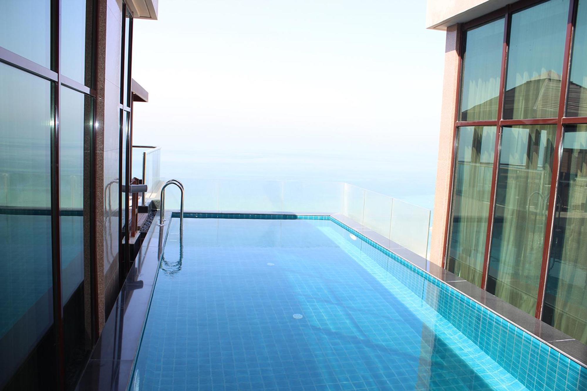 Lagoona Beach Luxury Resort And Spa Μανάμα Εξωτερικό φωτογραφία The photo shows an infinity pool situated on a balcony or rooftop, with a clear view extending to the horizon. The pool has a sleek design with blue tiles, and it appears to be reflecting the sky. There is a ladder on one side for access into the poo
