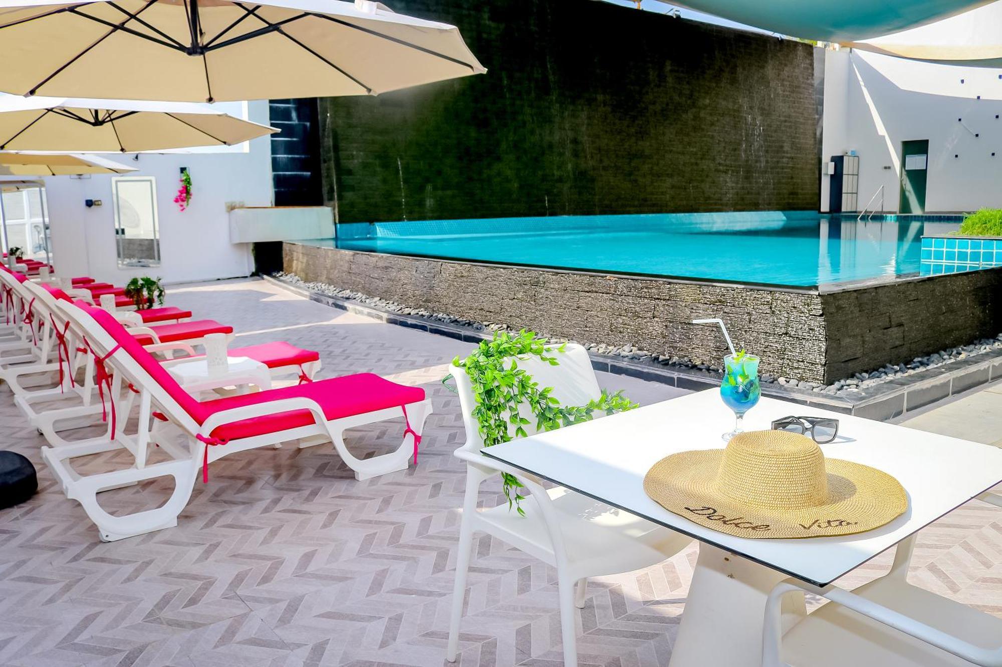 Lagoona Beach Luxury Resort And Spa Μανάμα Εξωτερικό φωτογραφία The photo shows a sunny poolside area with bright red lounge chairs arranged neatly beside a swimming pool. There are large beige umbrellas providing shade. A small table is set up with a straw hat and a colorful drink, suggesting a relaxed, tropical