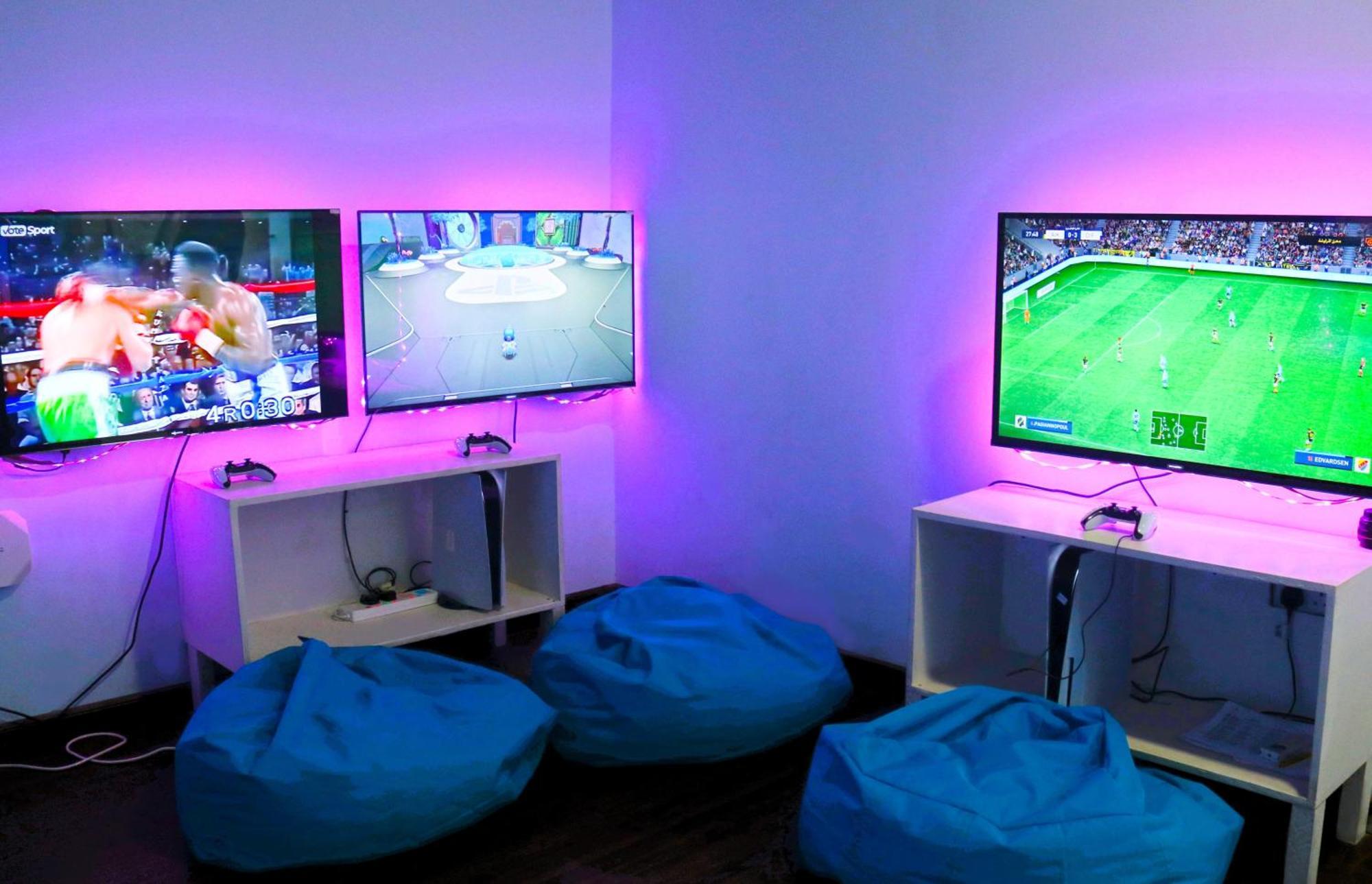 Lagoona Beach Luxury Resort And Spa Μανάμα Εξωτερικό φωτογραφία The photo shows a gaming area featuring three televisions mounted on the wall, displaying different games. Two of the TVs are showing gaming scenes, with one depicting a boxing game and the other showing a vibrant game environment. The third TV displ
