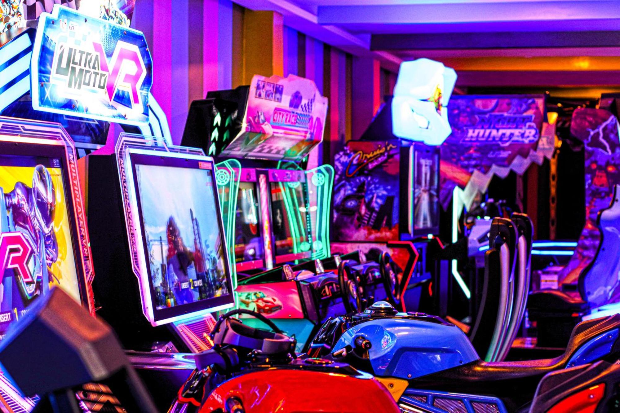 Lagoona Beach Luxury Resort And Spa Μανάμα Εξωτερικό φωτογραφία The photo shows a vibrant arcade scene featuring various arcade gaming machines. The machines are lined up, showcasing colorful screens and bright, neon lights, creating an energetic atmosphere. Some machines appear to be racing games, as indicated b