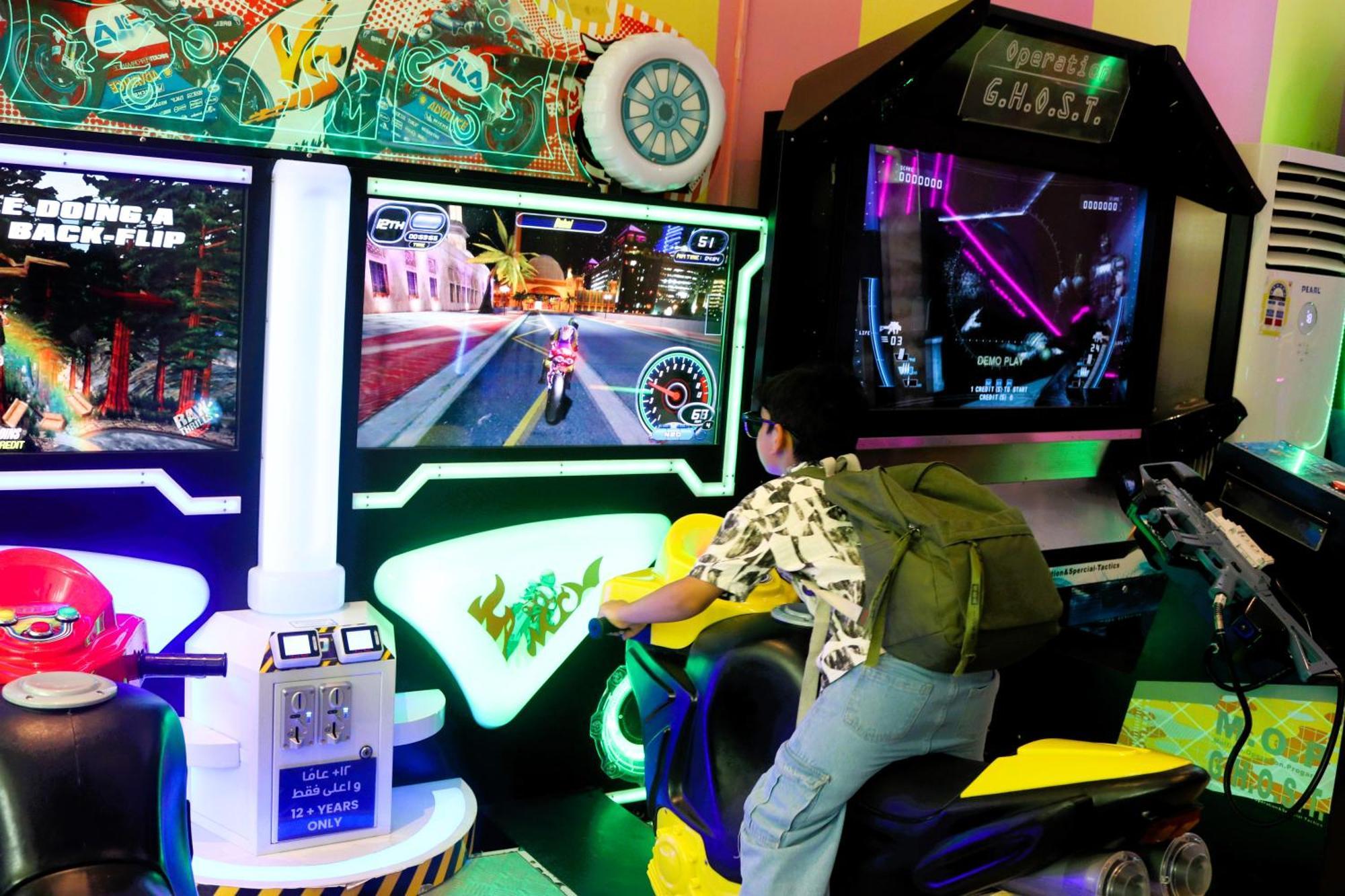 Lagoona Beach Luxury Resort And Spa Μανάμα Εξωτερικό φωτογραφία The photo shows a person playing an arcade motorcycle racing game. They are seated on a motorcycle-shaped seat, actively engaging with the game displayed on the screen in front of them. The screen shows a vibrant racing scene with streets and colorfu