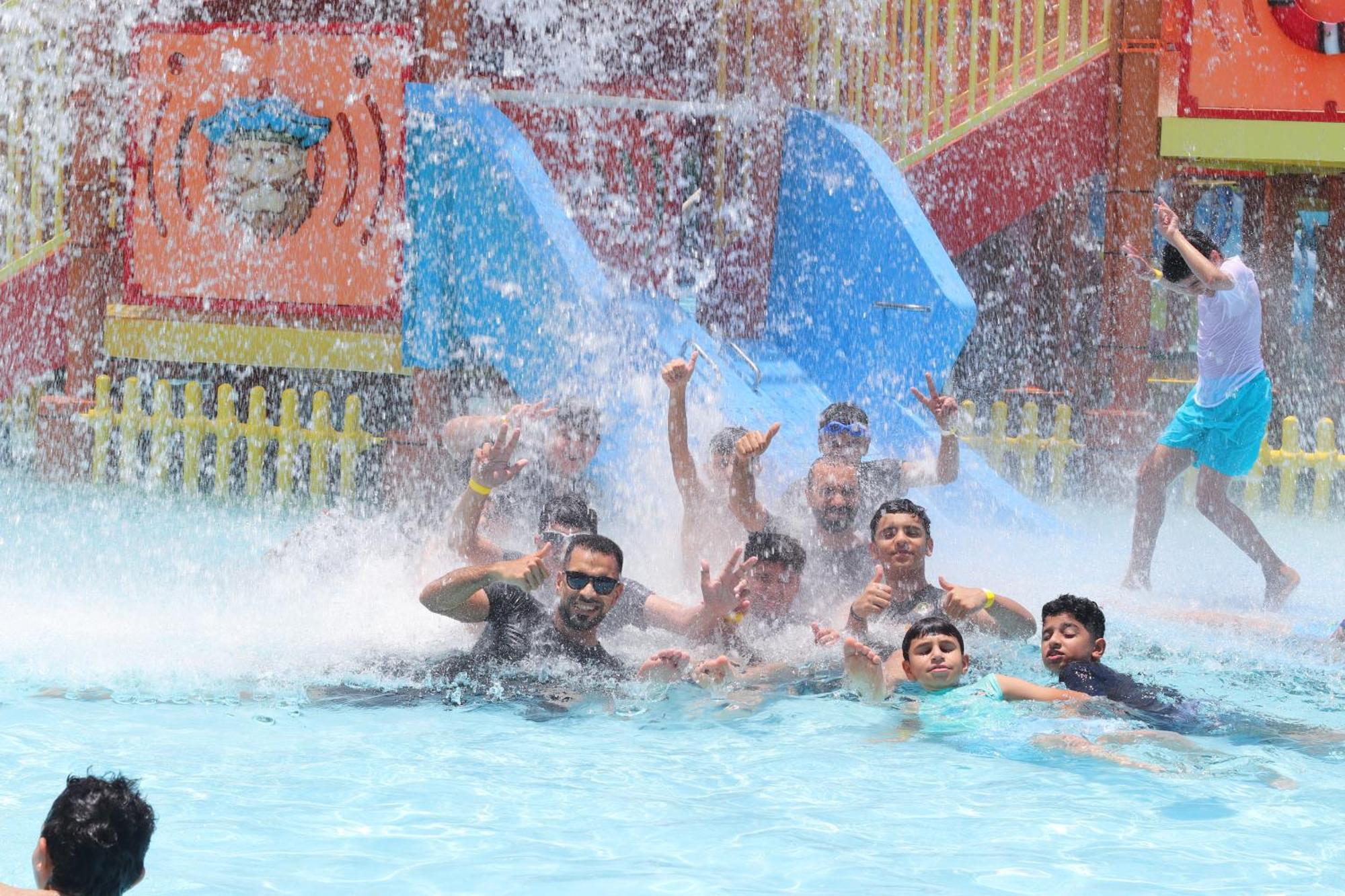 Lagoona Beach Luxury Resort And Spa Μανάμα Εξωτερικό φωτογραφία The photo shows a lively scene at a water park or pool area. Several people, including adults and children, are enjoying themselves in the water, splashing and posing for the camera. Water is cascading down, creating a refreshing atmosphere. In the b