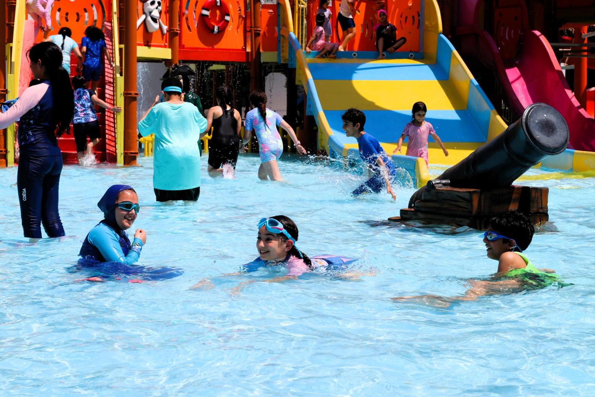 Lagoona Beach Luxury Resort And Spa Μανάμα Εξωτερικό φωτογραφία The photo shows a vibrant water park scene with several children playing in a shallow pool. Some are swimming and splashing around, while others are playing on colorful slides in the background. The atmosphere is lively and cheerful, with kids of var
