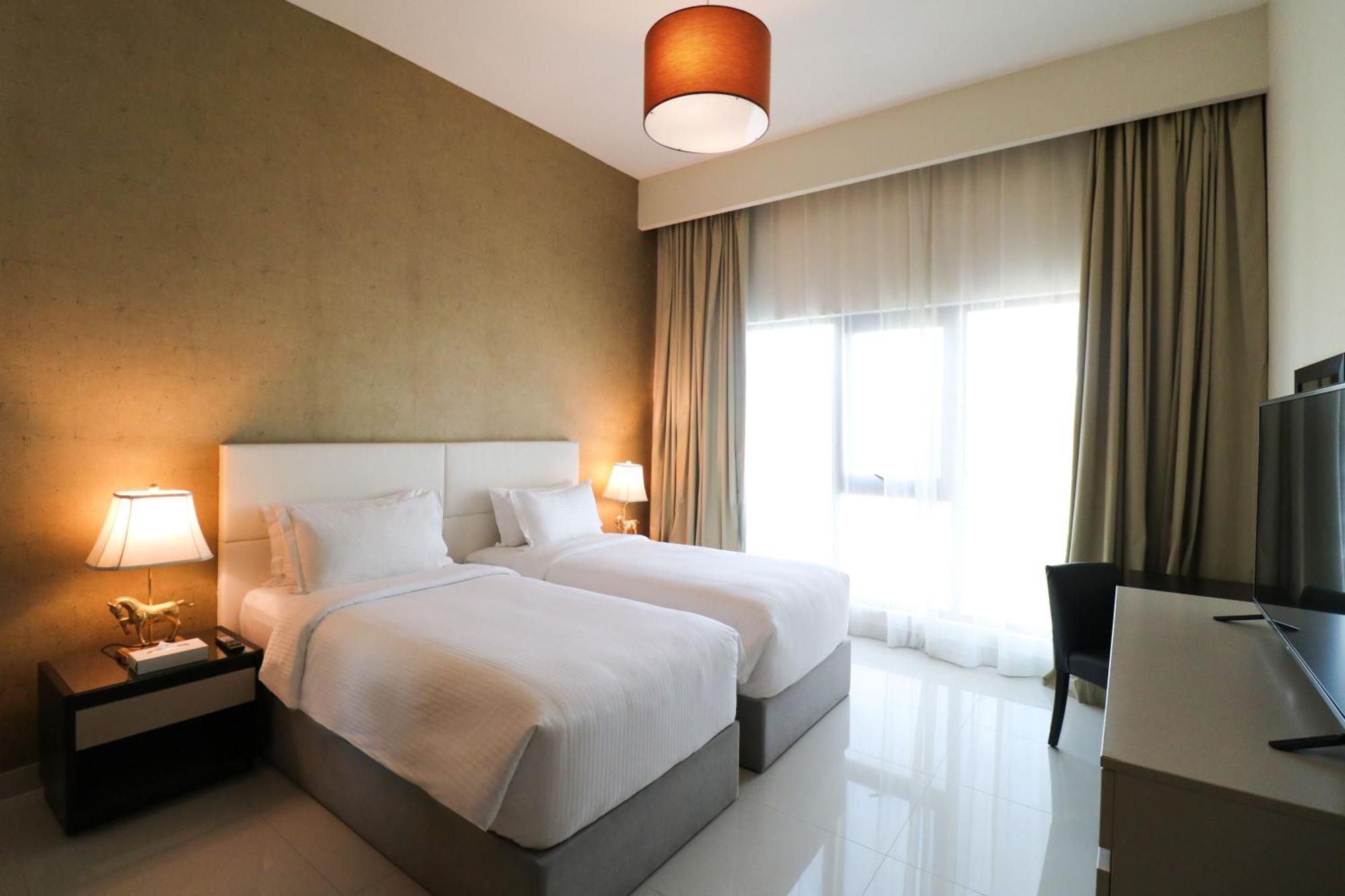 Lagoona Beach Luxury Resort And Spa Μανάμα Εξωτερικό φωτογραφία The photo shows a hotel room featuring two single beds with white bedding. The walls have a neutral tone, and there's a large window covered by light, sheer curtains allowing natural light to enter. On either side of the beds, there are bedside table